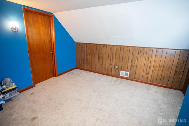 bonus room featuring lofted ceiling, light carpet, and wooden walls