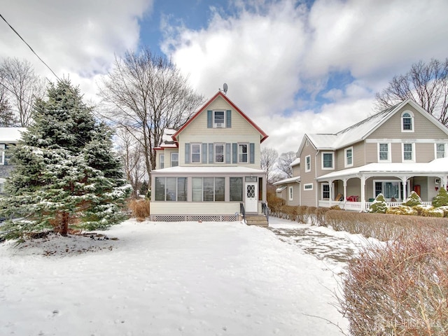 snow covered back of property with a porch and a sunroom