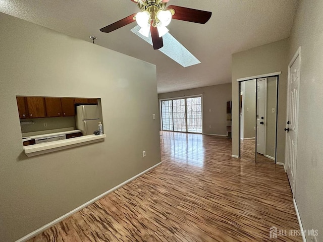 unfurnished room with a skylight, ceiling fan, and light wood-type flooring