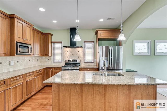 kitchen featuring pendant lighting, appliances with stainless steel finishes, sink, and wall chimney range hood