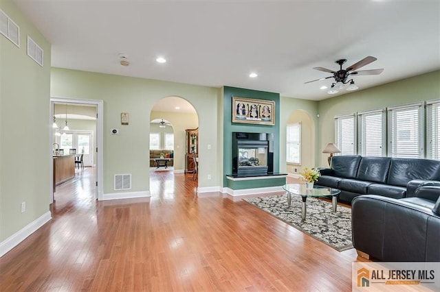 living room featuring ceiling fan, hardwood / wood-style flooring, a healthy amount of sunlight, and a multi sided fireplace