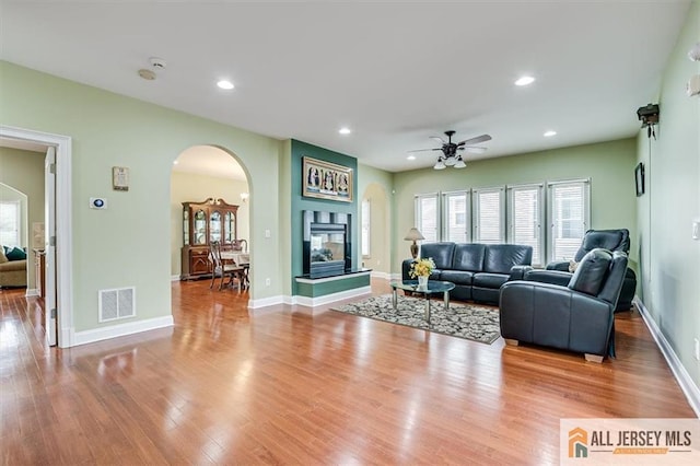 living room with ceiling fan, a multi sided fireplace, and light wood-type flooring