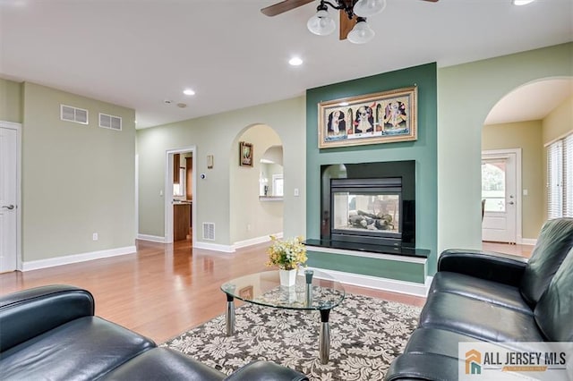 living room with light wood-type flooring, ceiling fan, and a multi sided fireplace