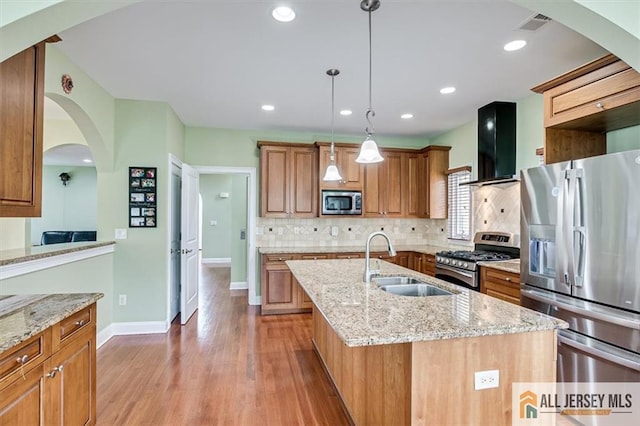 kitchen featuring an island with sink, appliances with stainless steel finishes, light stone counters, and wall chimney exhaust hood