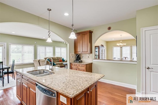 kitchen with hanging light fixtures, an island with sink, sink, and stainless steel dishwasher