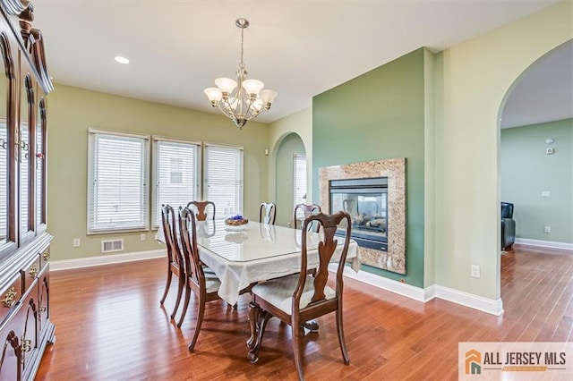 dining room featuring hardwood / wood-style floors, a notable chandelier, and a multi sided fireplace