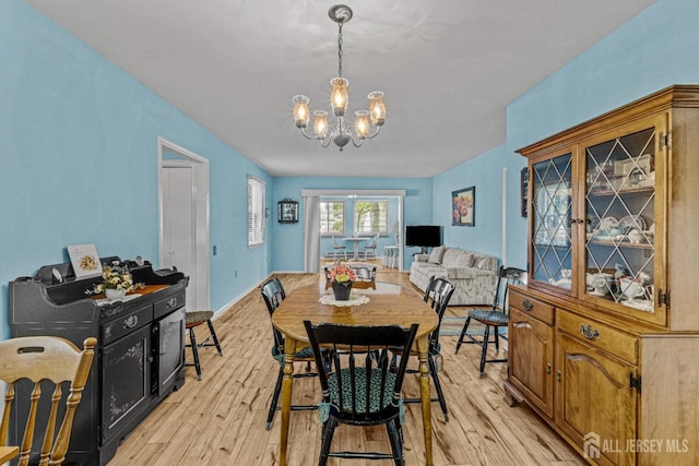 dining area with light wood-type flooring, an inviting chandelier, and baseboards