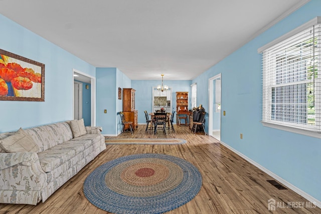 living area featuring baseboards, wood-type flooring, visible vents, and a notable chandelier