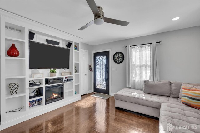 living room featuring built in shelves, wood-type flooring, and ceiling fan