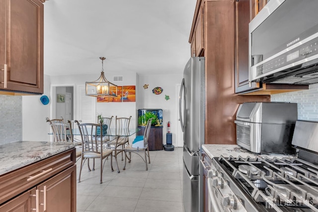 kitchen featuring hanging light fixtures, light stone counters, light tile patterned flooring, an inviting chandelier, and stainless steel appliances