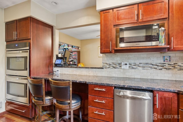kitchen with dark stone countertops, appliances with stainless steel finishes, wood finished floors, and backsplash