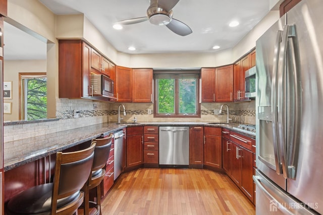 kitchen with a ceiling fan, a sink, light wood-style floors, dark stone counters, and appliances with stainless steel finishes