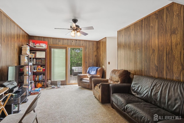 carpeted living room with ceiling fan and wood walls
