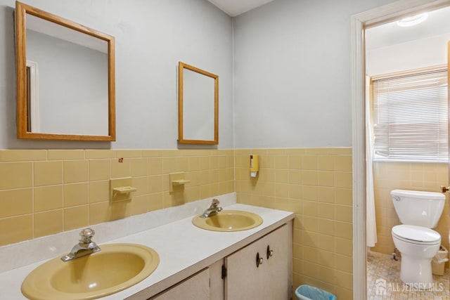 full bathroom with double vanity, tile walls, toilet, and a sink