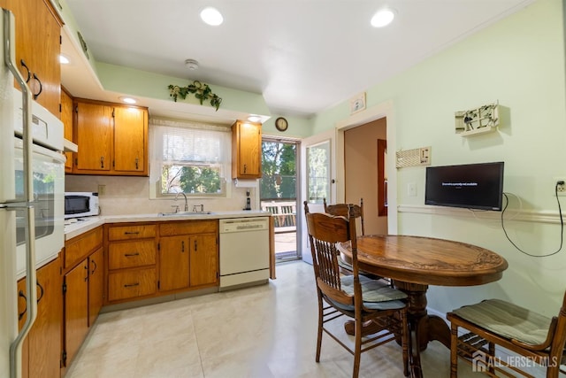 kitchen with light countertops, a sink, brown cabinets, and white appliances