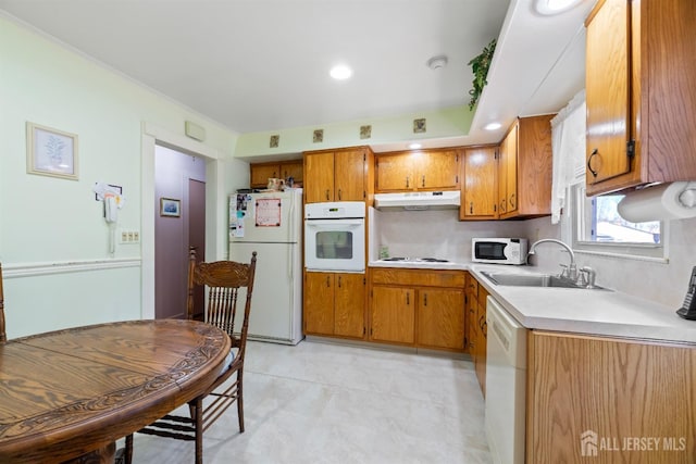 kitchen featuring a sink, light countertops, under cabinet range hood, white appliances, and brown cabinetry