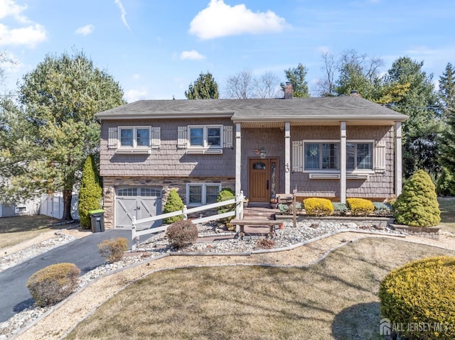 split foyer home featuring roof with shingles, a chimney, aphalt driveway, and an attached garage