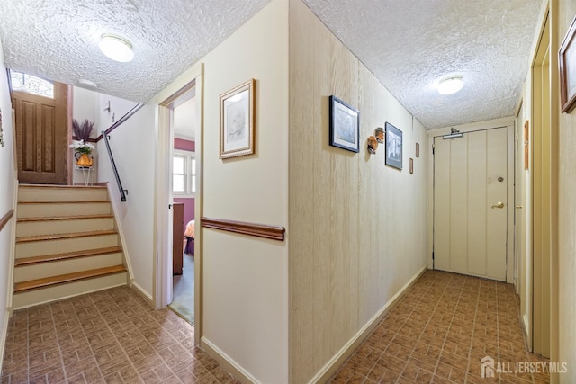 hallway featuring a textured ceiling, brick patterned floor, stairway, and baseboards