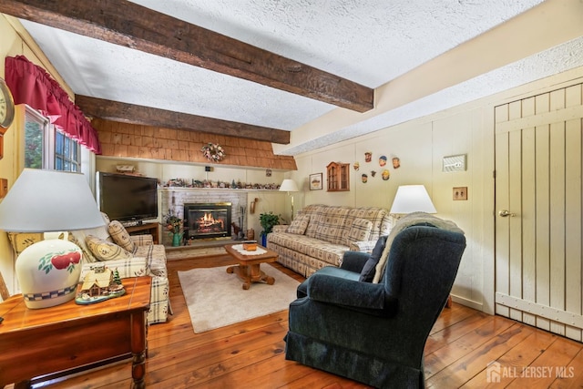 living area with beam ceiling, a fireplace, a textured ceiling, and wood-type flooring