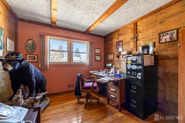 office with wood finished floors, wood walls, beam ceiling, visible vents, and a textured ceiling