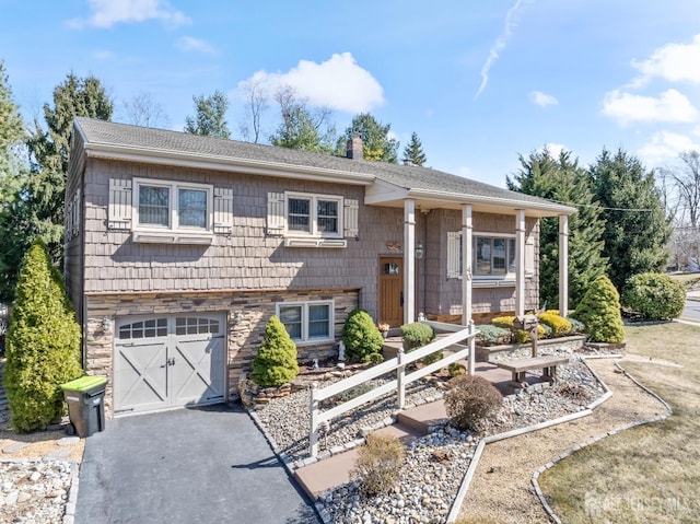 split foyer home with a garage, a shingled roof, a chimney, stone siding, and aphalt driveway