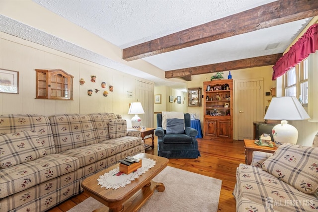 living room with a textured ceiling, visible vents, beam ceiling, and hardwood / wood-style flooring