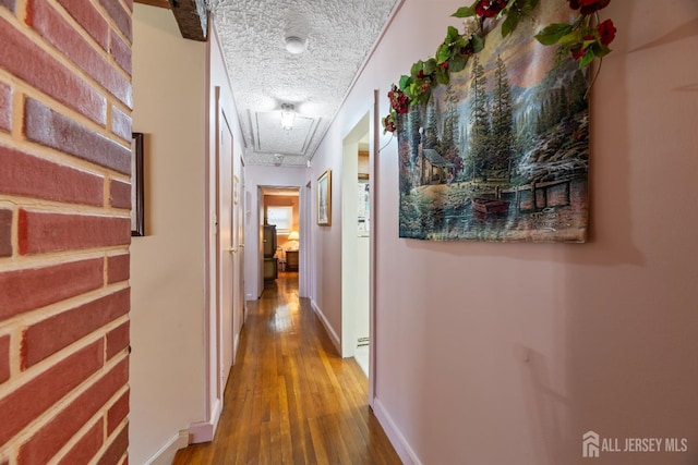 hallway with baseboards, attic access, a textured ceiling, and wood finished floors
