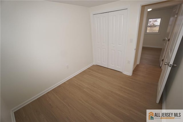 unfurnished bedroom featuring wood finished floors, a closet, and baseboards