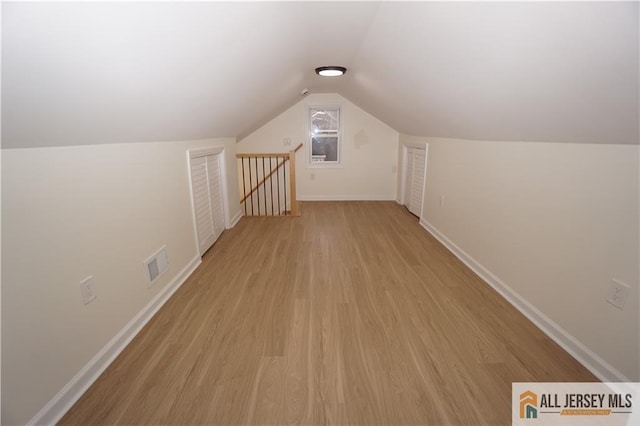 additional living space featuring vaulted ceiling, light wood-style floors, visible vents, and baseboards