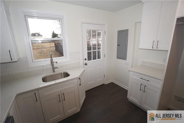 kitchen with tasteful backsplash, light countertops, electric panel, white cabinetry, and a sink