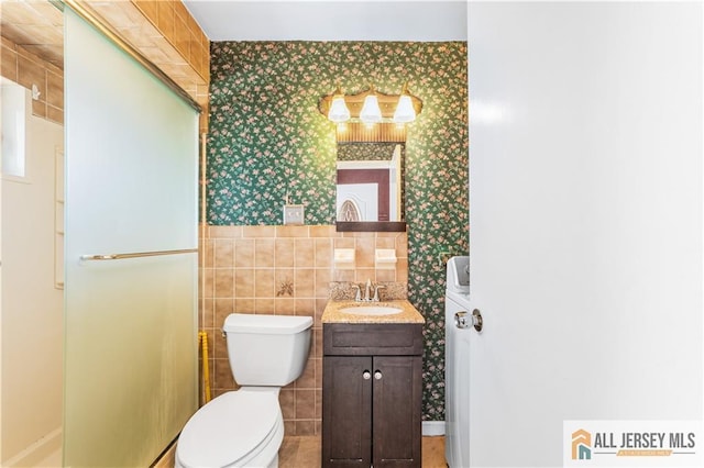 bathroom with wallpapered walls, toilet, tile walls, and vanity
