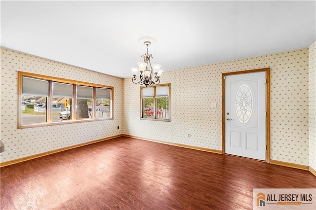 entrance foyer featuring wallpapered walls, wood finished floors, a chandelier, and baseboards