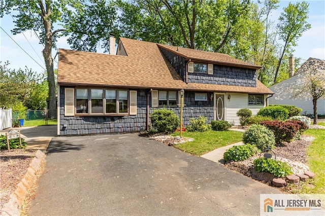 view of front of home with driveway, fence, a chimney, and a shingled roof