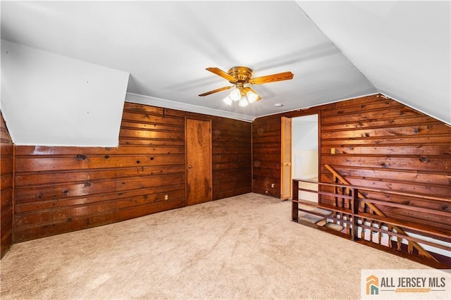 additional living space featuring a ceiling fan, carpet flooring, wooden walls, and vaulted ceiling