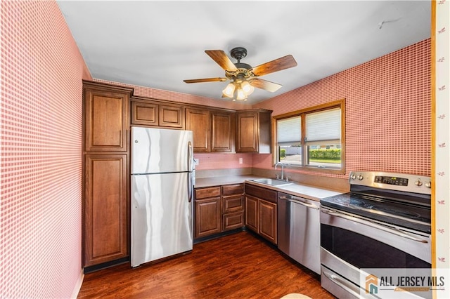 kitchen featuring appliances with stainless steel finishes, wallpapered walls, a sink, dark wood finished floors, and a ceiling fan
