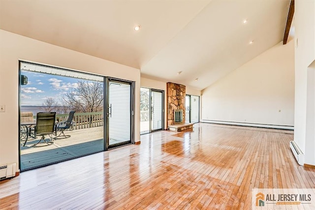 spare room with light wood-type flooring, high vaulted ceiling, a baseboard heating unit, a stone fireplace, and baseboard heating