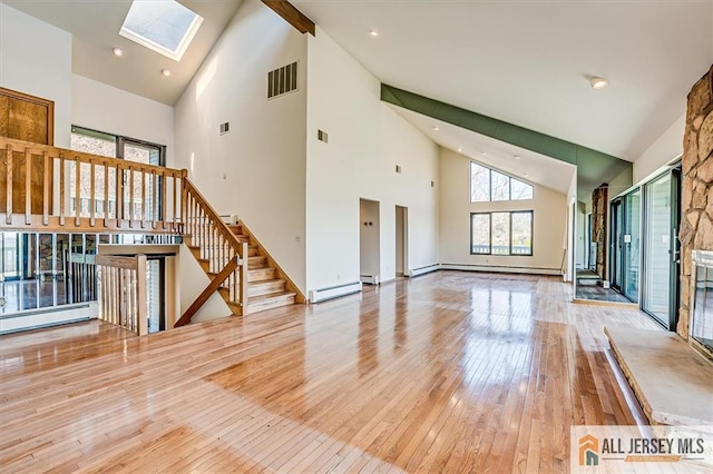 unfurnished living room with visible vents, stairway, a skylight, light wood-style floors, and a baseboard radiator