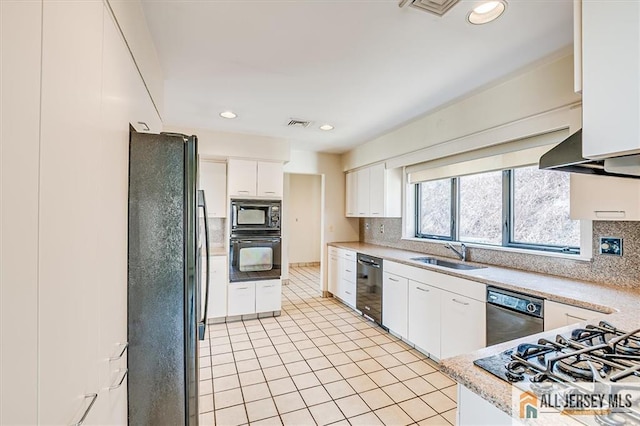 kitchen with a sink, decorative backsplash, black appliances, light countertops, and wall chimney range hood