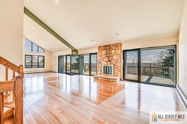 unfurnished living room featuring a wealth of natural light, wood-type flooring, high vaulted ceiling, and a stone fireplace