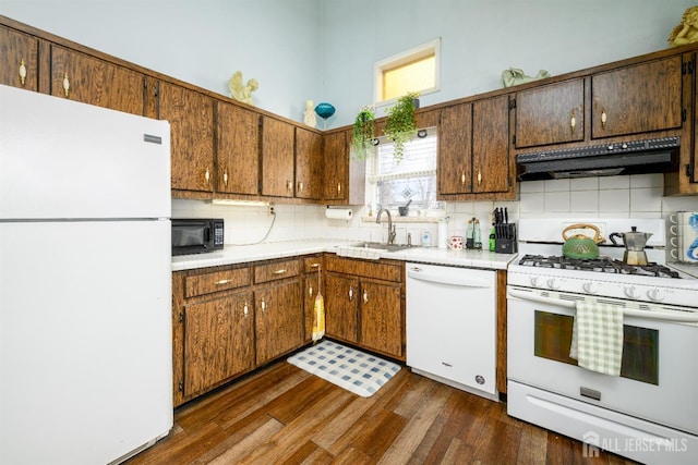 kitchen featuring dark wood-style floors, a sink, tasteful backsplash, white appliances, and premium range hood