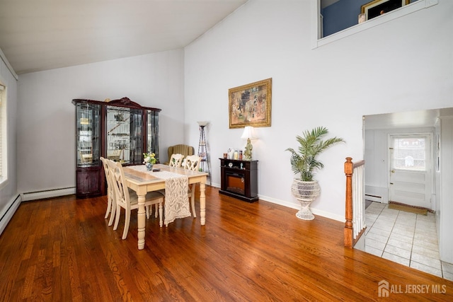 dining space featuring a baseboard heating unit, wood finished floors, baseboards, and high vaulted ceiling