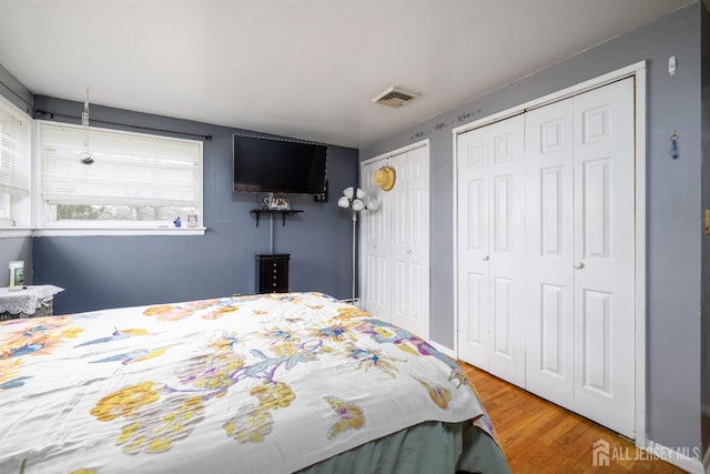 bedroom featuring wood finished floors, multiple closets, and visible vents