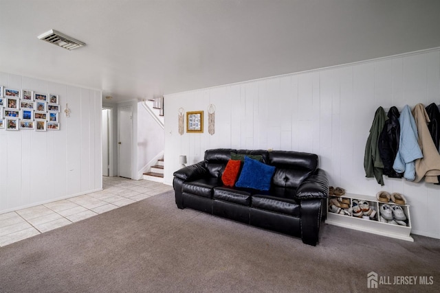 carpeted living room with tile patterned floors, baseboards, visible vents, stairway, and wooden walls