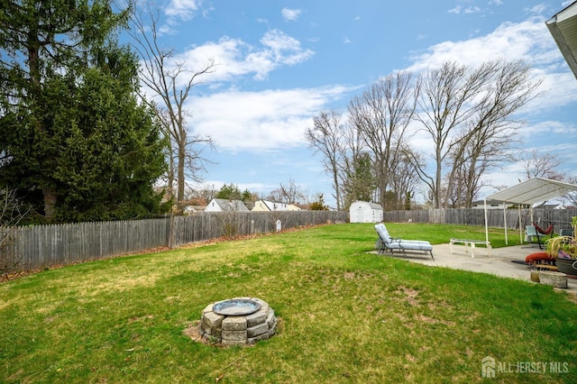 view of yard featuring a storage unit, a fenced backyard, a fire pit, an outdoor structure, and a patio