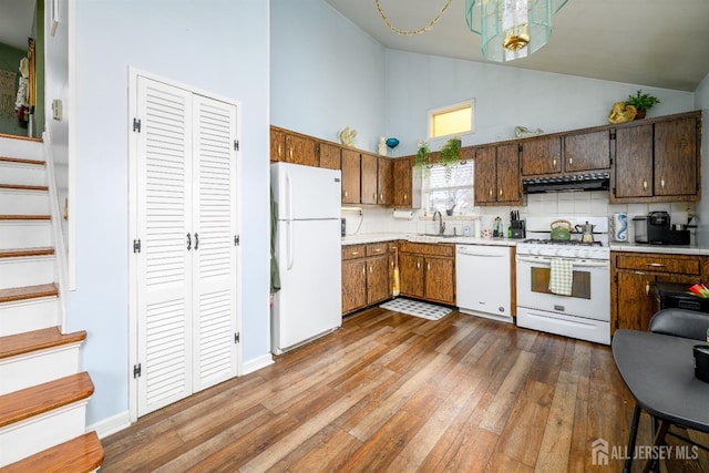 kitchen featuring high vaulted ceiling, wood finished floors, white appliances, light countertops, and under cabinet range hood