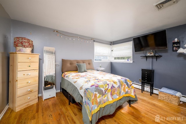 bedroom with baseboard heating, baseboards, wood finished floors, and visible vents
