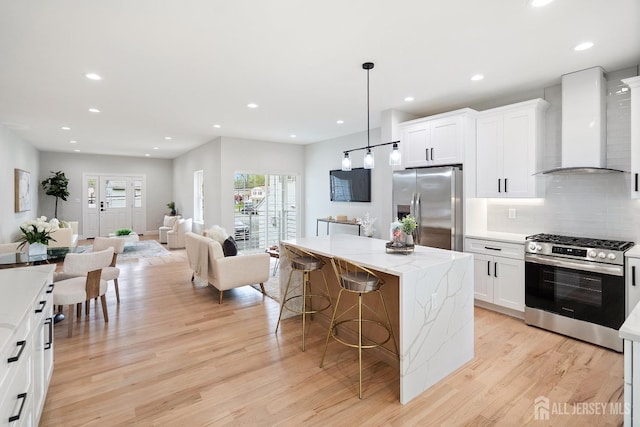 695 Inman Ave, Colonia, NJ 07067 - kitchen featuring appliances with stainless steel finishes, wall chimney exhaust hood, light wood finished floors, a center island, and a breakfast bar