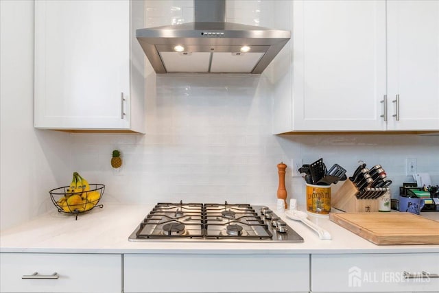 kitchen featuring stainless steel gas stovetop, white cabinetry, decorative backsplash, and wall chimney exhaust hood