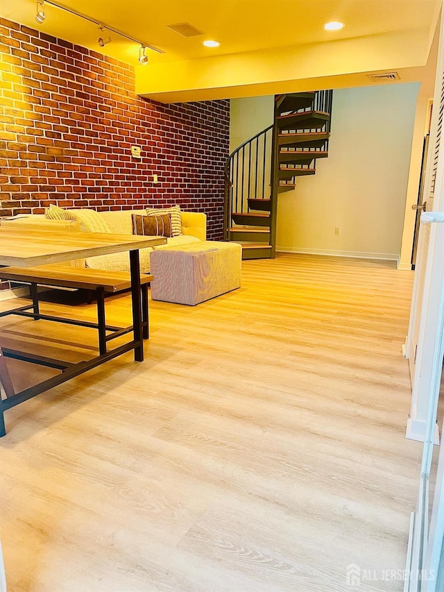 interior space with hardwood / wood-style flooring, rail lighting, and brick wall