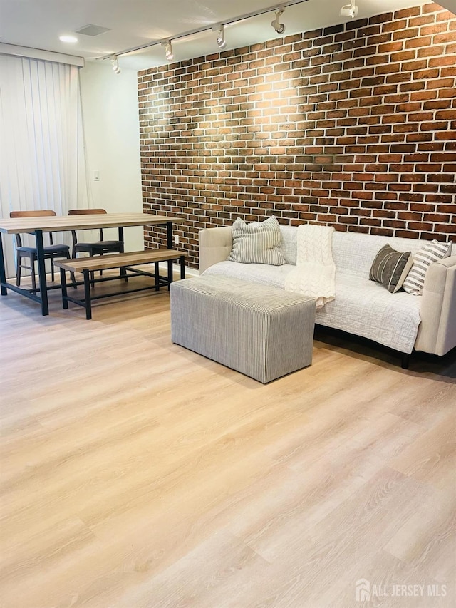 living room with light hardwood / wood-style flooring, brick wall, and track lighting